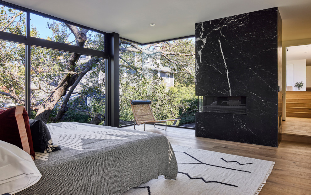 Design ideas for a large modern master and grey and black bedroom in Los Angeles with grey walls, light hardwood flooring, a corner fireplace, a stone fireplace surround, beige floors and all types of wall treatment.
