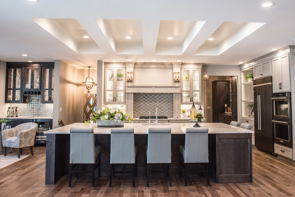Open concept kitchen - huge transitional l-shaped medium tone wood floor and brown floor open concept kitchen idea with a single-bowl sink, glass-front cabinets, gray cabinets, quartz countertops, gray backsplash, ceramic backsplash, stainless steel appliances, an island and white countertops