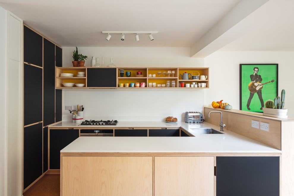 This is an example of a mid-sized midcentury u-shaped kitchen in London with an undermount sink, flat-panel cabinets, stainless steel appliances, orange floor, white benchtop, black cabinets and a peninsula.