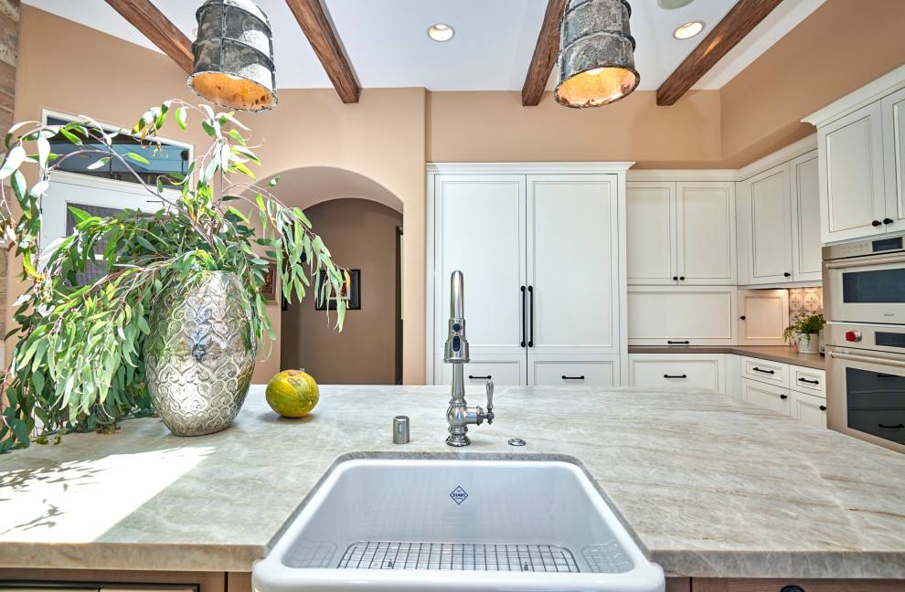 Open concept kitchen - mid-sized rustic galley travertine floor, beige floor and exposed beam open concept kitchen idea in Denver with a farmhouse sink, recessed-panel cabinets, white cabinets, quartz countertops, multicolored backsplash, stone tile backsplash, stainless steel appliances, an island and brown countertops