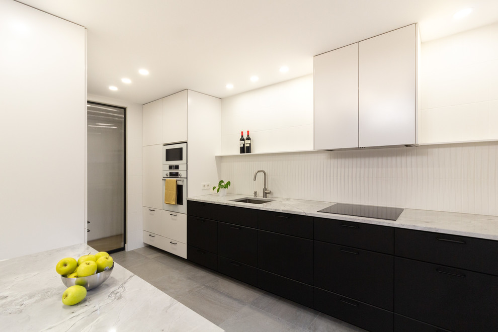 Design ideas for a mid-sized contemporary single-wall open plan kitchen in Madrid with an undermount sink, flat-panel cabinets, black cabinets, quartzite benchtops, white splashback, ceramic splashback, panelled appliances, ceramic floors, no island, grey floor and white benchtop.
