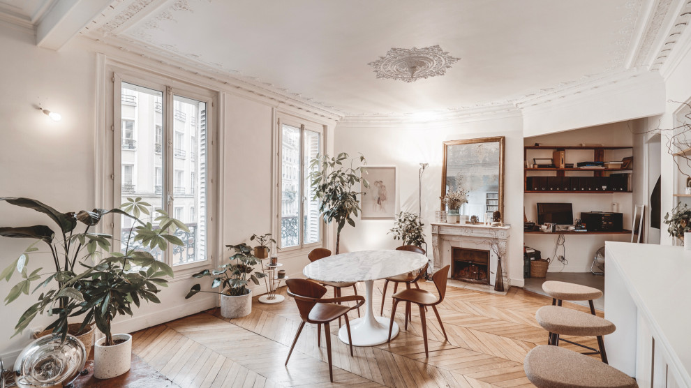 Photo of a mid-sized scandinavian open plan dining in Paris with white walls, medium hardwood floors, a standard fireplace, brown floor, a stone fireplace surround and decorative wall panelling.