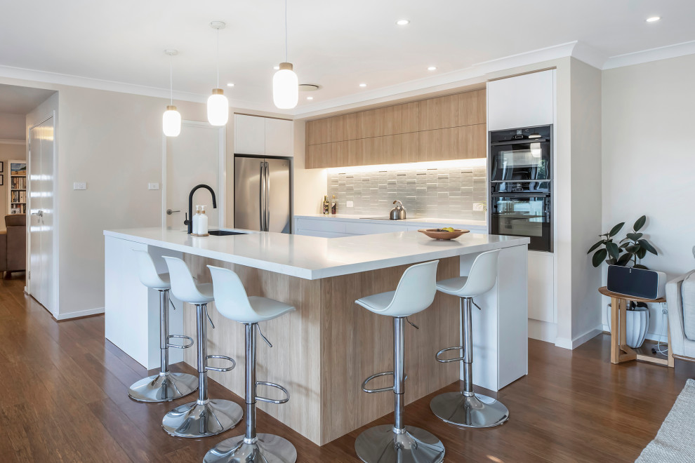 Design ideas for a mid-sized contemporary galley open plan kitchen in Sydney with an undermount sink, flat-panel cabinets, white cabinets, quartz benchtops, green splashback, porcelain splashback, black appliances, medium hardwood floors, with island and white benchtop.