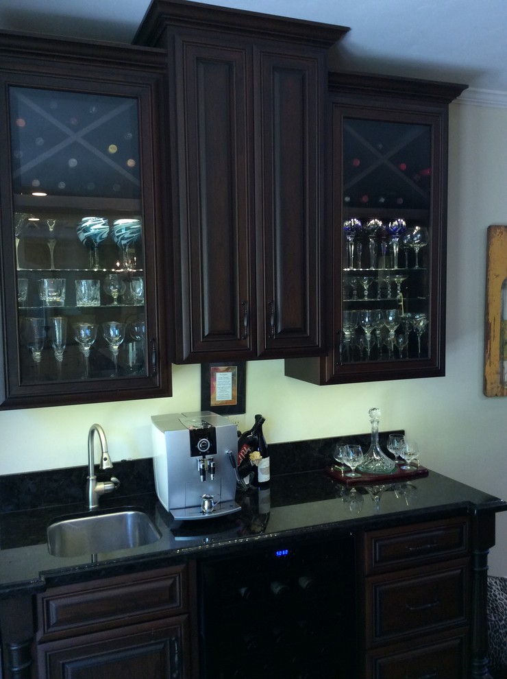 This is an example of a small traditional galley kitchen pantry in San Francisco with an undermount sink, raised-panel cabinets, dark wood cabinets, granite benchtops, black splashback, stone slab splashback, black appliances and dark hardwood floors.