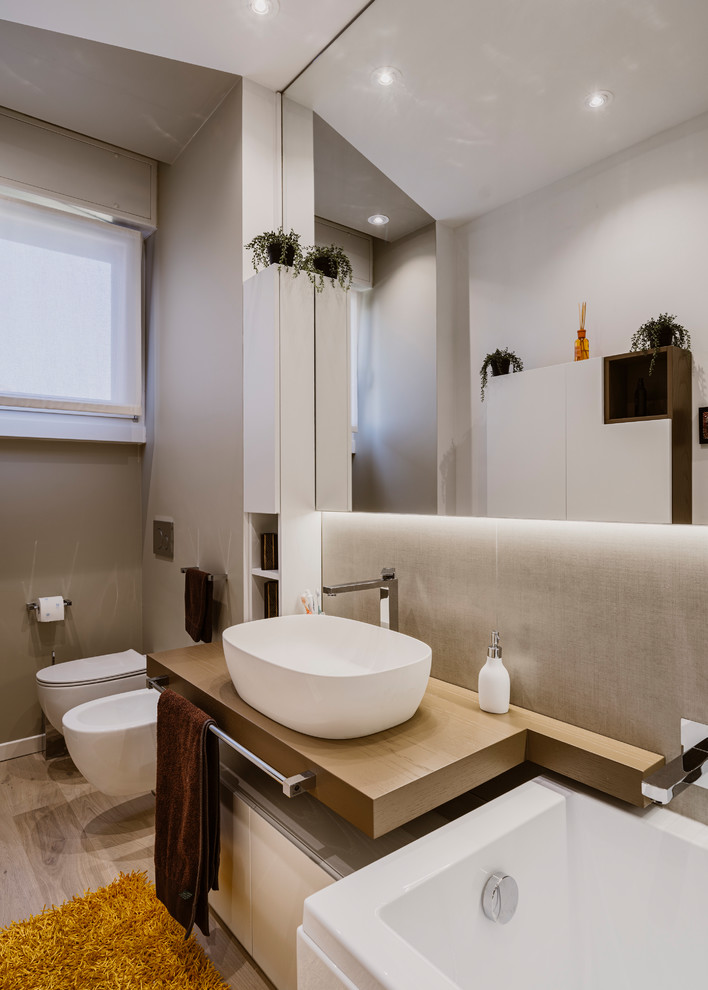 Design ideas for a small modern 3/4 bathroom in Milan with flat-panel cabinets, beige cabinets, a corner tub, an alcove shower, a two-piece toilet, beige tile, porcelain tile, beige walls, light hardwood floors, a vessel sink, wood benchtops, beige floor, a sliding shower screen and brown benchtops.
