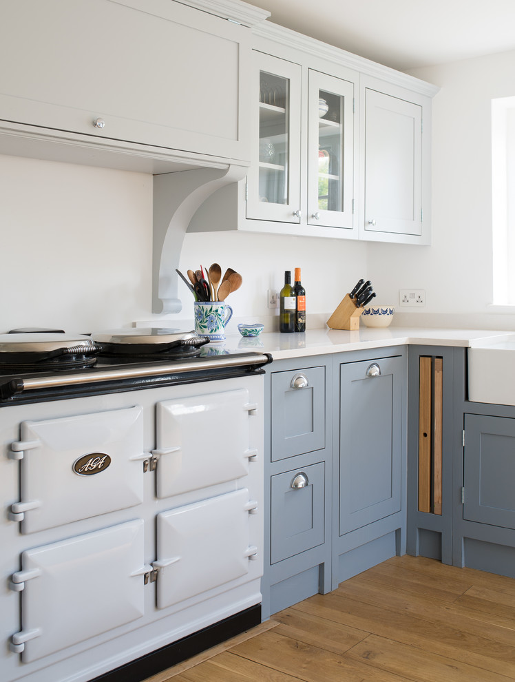 Photo of a mid-sized country kitchen in Gloucestershire with shaker cabinets, blue cabinets, quartzite benchtops, light hardwood floors, no island, a farmhouse sink and white appliances.