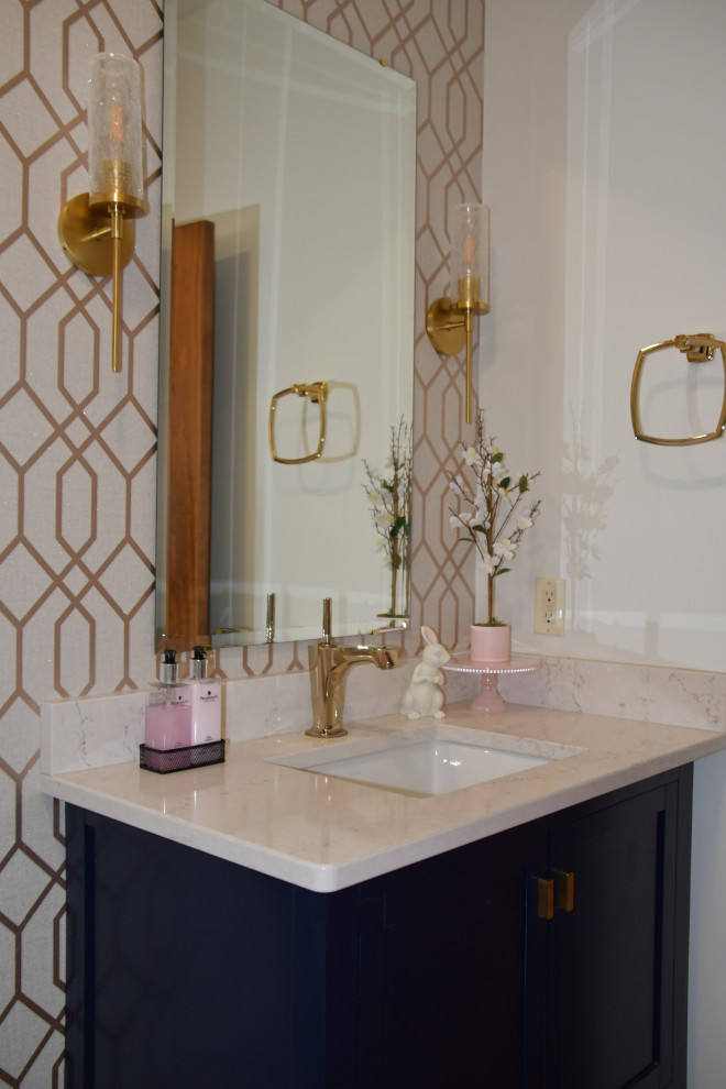 Small modern cloakroom in Milwaukee with flat-panel cabinets, blue cabinets, a two-piece toilet, beige walls, medium hardwood flooring, a submerged sink, engineered stone worktops, brown floors, beige worktops, a freestanding vanity unit and wallpapered walls.