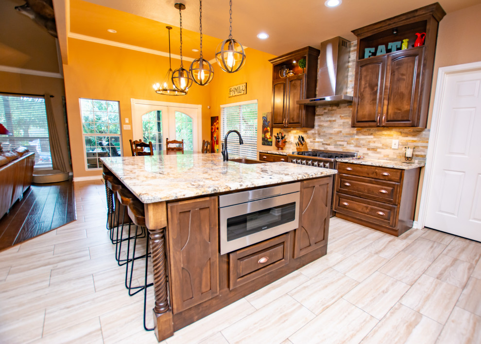 Transitional porcelain tile and beige floor kitchen photo in Austin with a farmhouse sink, raised-panel cabinets, dark wood cabinets, granite countertops, stone tile backsplash, stainless steel appliances and an island