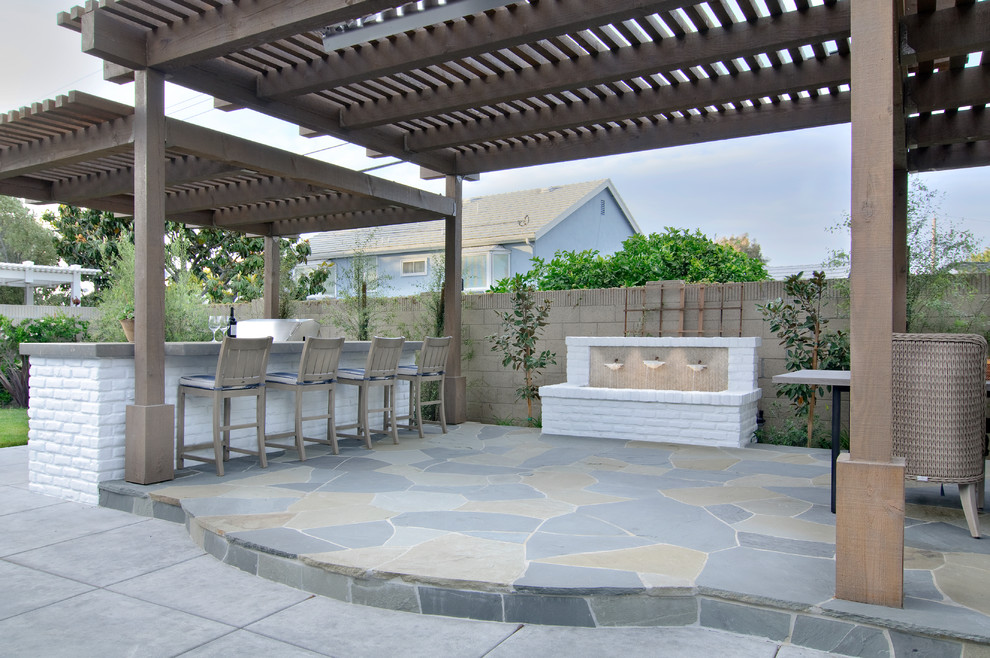 Inspiration for a large transitional backyard patio in Orange County with an outdoor kitchen, natural stone pavers and a pergola.