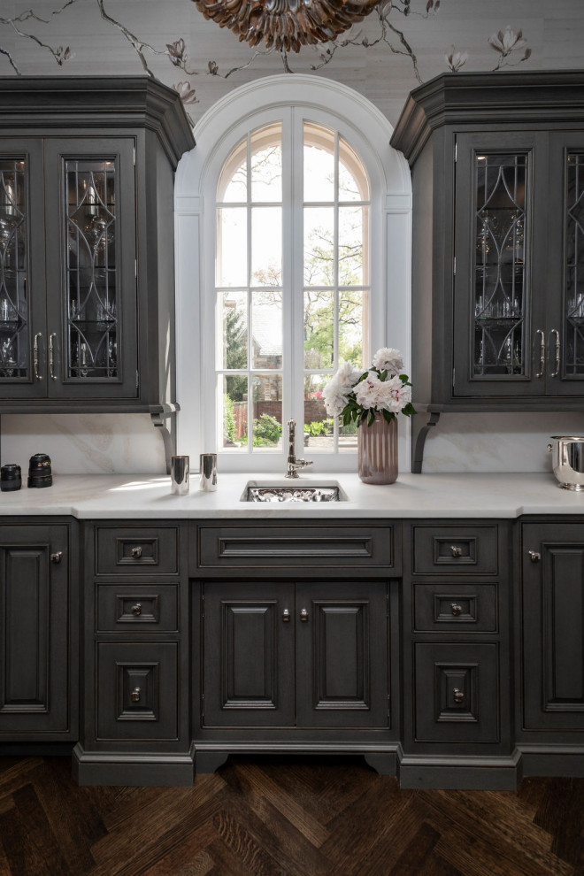 Example of a classic single-wall dark wood floor and brown floor wet bar design in Baltimore with an undermount sink, dark wood cabinets, marble countertops, white backsplash, marble backsplash and white countertops