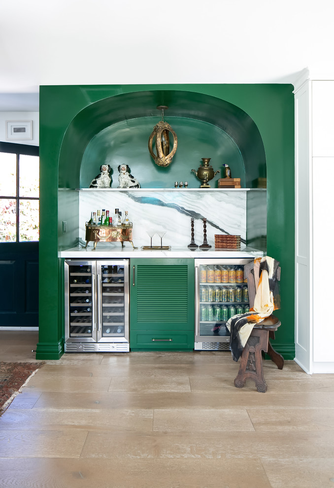 Inspiration for a beach style single-wall home bar in Orange County with no sink, louvered cabinets, green cabinets, multi-coloured splashback, light hardwood floors, white benchtop and stone slab splashback.