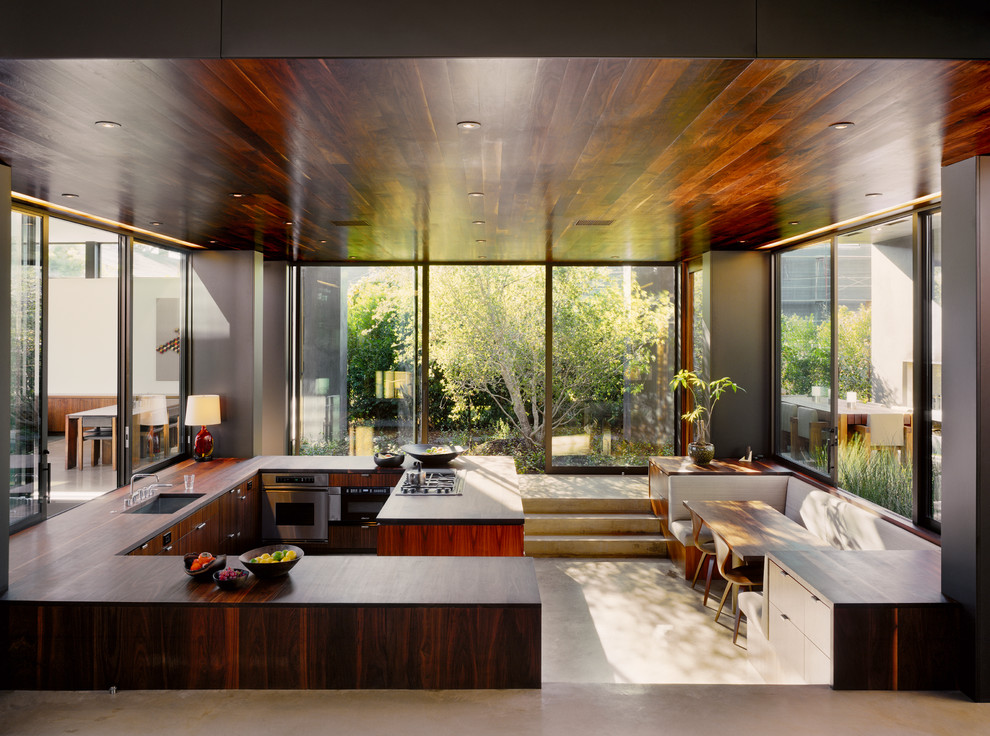 This is an example of a modern u-shaped eat-in kitchen in Los Angeles with an undermount sink, flat-panel cabinets, dark wood cabinets, stainless steel appliances and concrete floors.