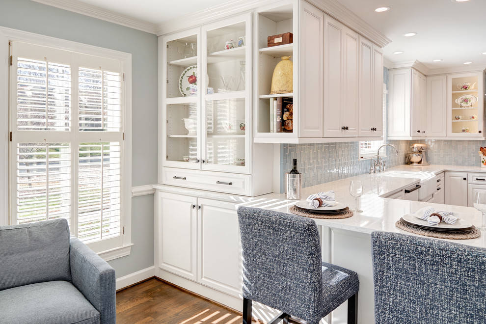 Inspiration for a mid-sized transitional u-shaped eat-in kitchen in Other with a farmhouse sink, raised-panel cabinets, white cabinets, quartz benchtops, blue splashback, porcelain splashback, panelled appliances, medium hardwood floors, with island and brown floor.
