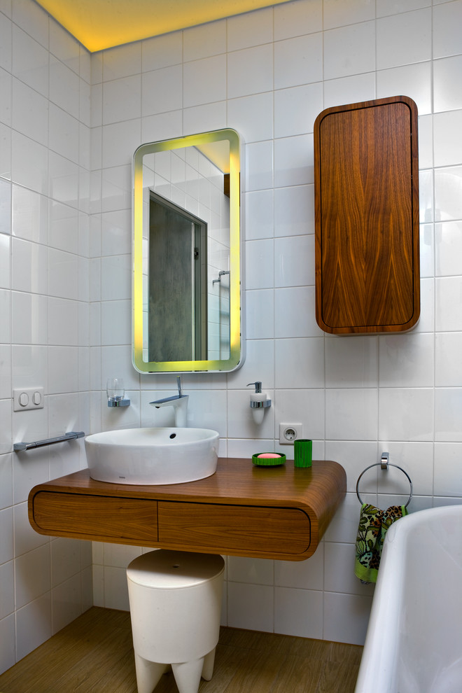 This is an example of a contemporary kids bathroom in Saint Petersburg with flat-panel cabinets, medium wood cabinets, a claw-foot tub, white tile, a vessel sink, wood benchtops, white walls, medium hardwood floors and brown benchtops.