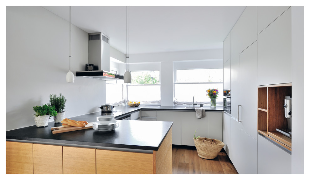 Design ideas for an expansive contemporary u-shaped open plan kitchen in Munich with white cabinets, white splashback, stainless steel appliances, a peninsula, an integrated sink, flat-panel cabinets, granite benchtops, window splashback, dark hardwood floors and brown floor.