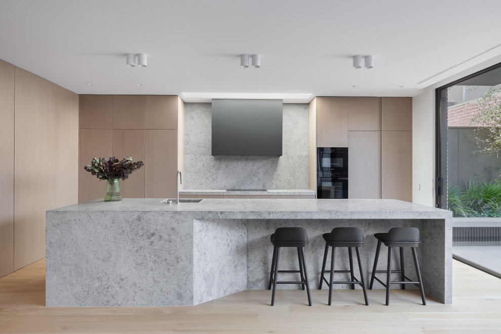Modern galley kitchen in Melbourne with an undermount sink, flat-panel cabinets, light wood cabinets, light hardwood floors, with island, beige floor and grey benchtop.