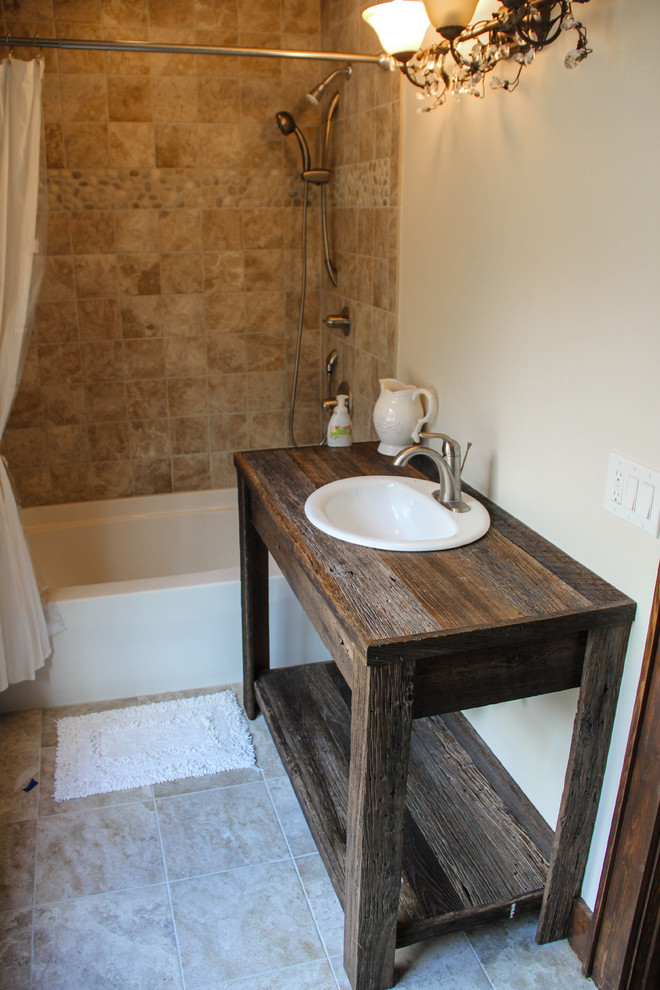 This is an example of a mid-sized country bathroom in Charlotte with a drop-in sink, open cabinets, wood benchtops, an alcove tub, a shower/bathtub combo, beige tile, beige walls, ceramic floors and dark wood cabinets.