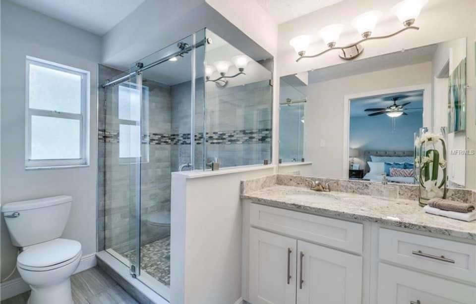 Design ideas for a transitional bathroom in Orlando with shaker cabinets, white cabinets, a one-piece toilet, white walls, an undermount sink, granite benchtops, a sliding shower screen and multi-coloured benchtops.