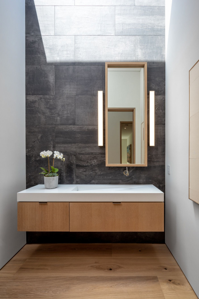 Inspiration for a contemporary powder room in Orange County with flat-panel cabinets, light wood cabinets, black tile, white walls, light hardwood floors, an integrated sink, beige floor, white benchtops and a floating vanity.
