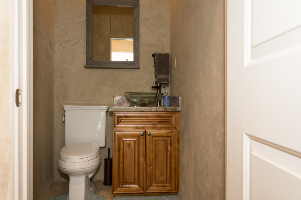 Inspiration for a small traditional powder room in Houston with raised-panel cabinets, medium wood cabinets, a one-piece toilet, brown walls, travertine floors, a vessel sink, granite benchtops and brown floor.