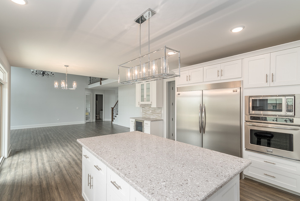 Inspiration for a large transitional u-shaped eat-in kitchen in Chicago with an undermount sink, white cabinets, stainless steel appliances, with island, recessed-panel cabinets, terrazzo benchtops, grey splashback, matchstick tile splashback, light hardwood floors, grey floor and grey benchtop.