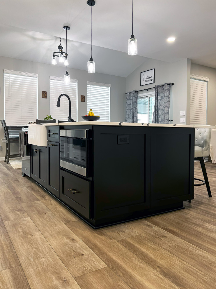 Example of a large transitional single-wall vinyl floor and beige floor eat-in kitchen design with a farmhouse sink, shaker cabinets, black cabinets, quartz countertops, black backsplash, subway tile backsplash, stainless steel appliances, an island and white countertops
