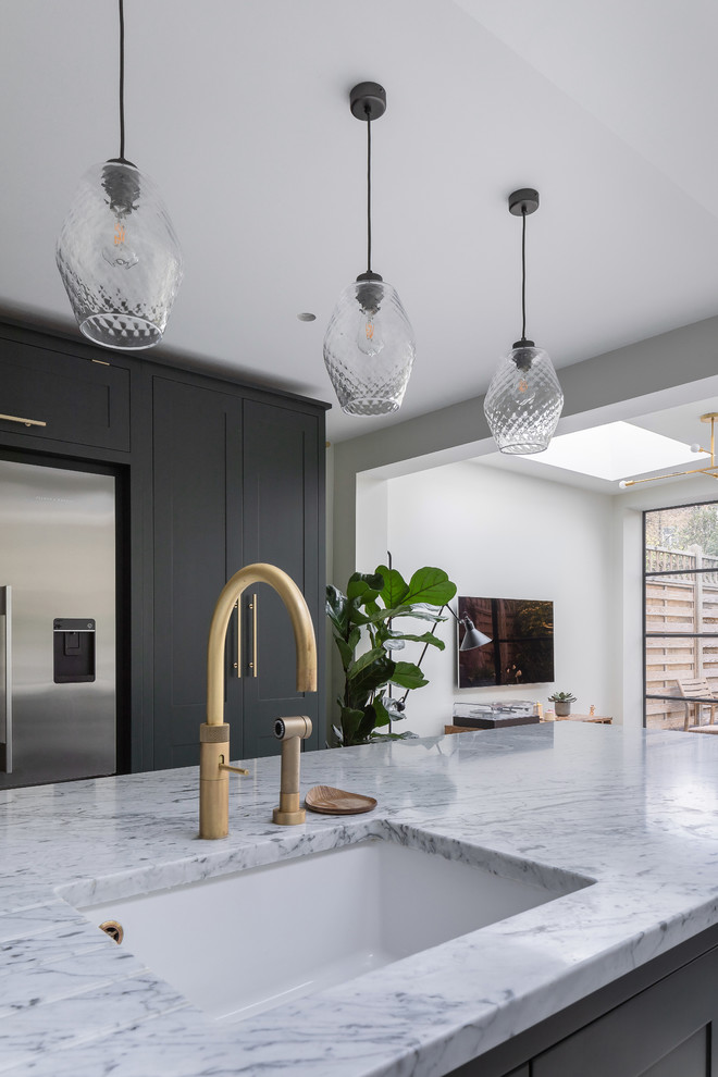 Mid-sized contemporary u-shaped eat-in kitchen in London with an integrated sink, shaker cabinets, green cabinets, marble benchtops, white splashback, marble splashback, stainless steel appliances, concrete floors, with island, grey floor and white benchtop.