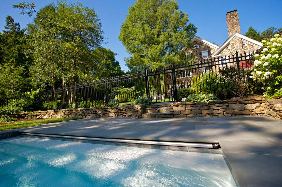 This is an example of a mid-sized traditional side yard rectangular pool in Philadelphia with natural stone pavers.