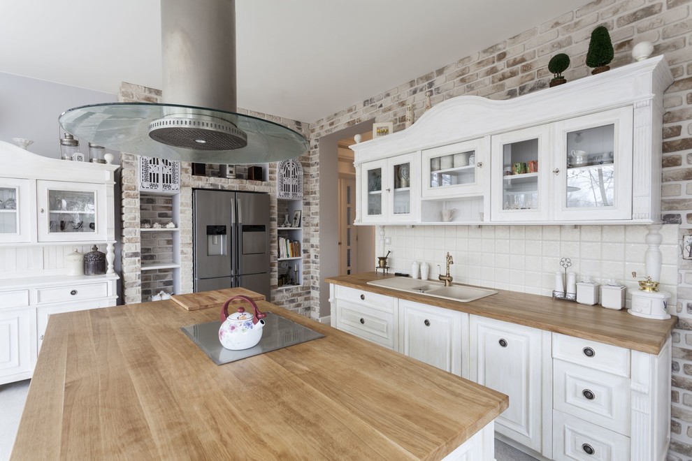 Photo of a country l-shaped separate kitchen in Los Angeles with a drop-in sink, raised-panel cabinets, white cabinets, white splashback, stainless steel appliances and with island.