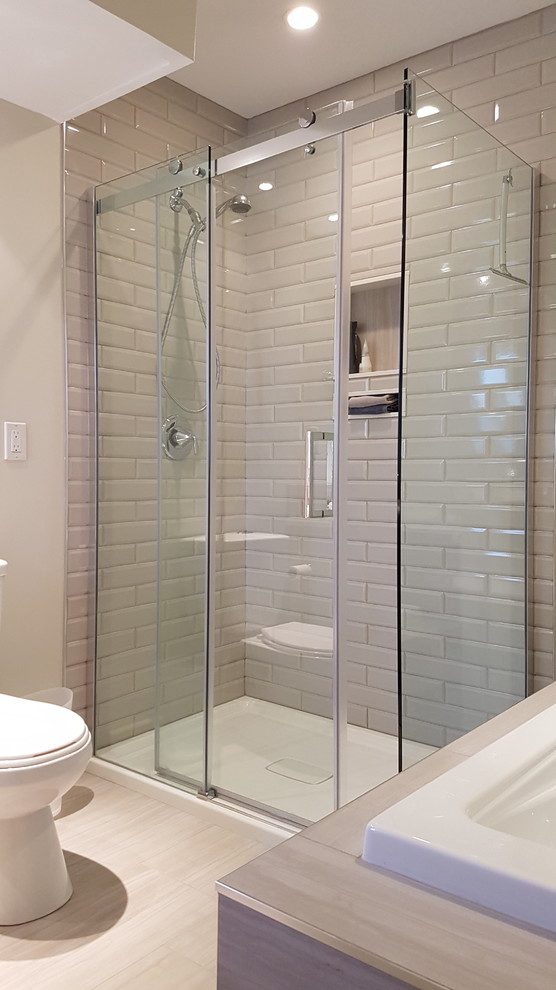 This is an example of a mid-sized contemporary master bathroom in Toronto with a drop-in tub, an alcove shower, a one-piece toilet, beige tile, ceramic tile, beige walls, laminate floors, laminate benchtops, beige floor and a sliding shower screen.