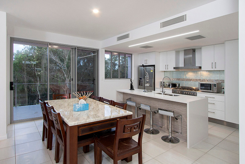 Photo of a mid-sized contemporary galley kitchen in Sunshine Coast with a drop-in sink, white cabinets, granite benchtops, metallic splashback, glass tile splashback, stainless steel appliances, ceramic floors and with island.