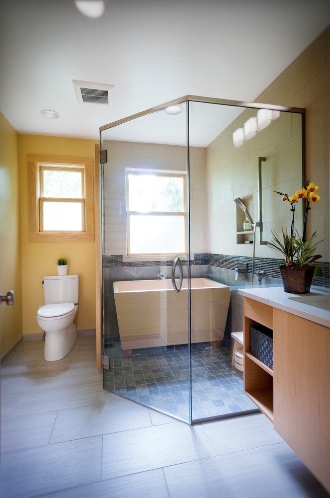 This is an example of a mid-sized asian master bathroom in Portland with flat-panel cabinets, light wood cabinets, gray tile, engineered quartz benchtops, white benchtops, a freestanding tub, a corner shower, a two-piece toilet, slate, white walls, porcelain floors, an undermount sink, grey floor and a hinged shower door.