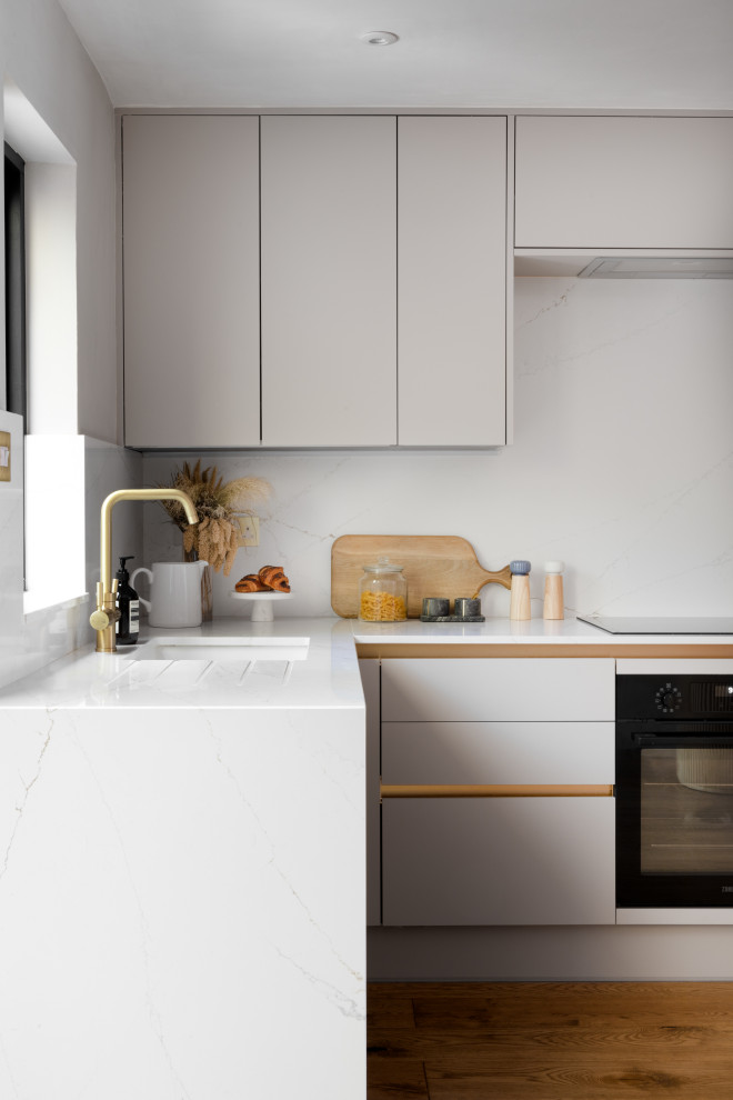 Inspiration for a small contemporary u-shaped open plan kitchen in Manchester with an integrated sink, flat-panel cabinets, beige cabinets, solid surface benchtops, white splashback, black appliances, light hardwood floors, no island and yellow benchtop.