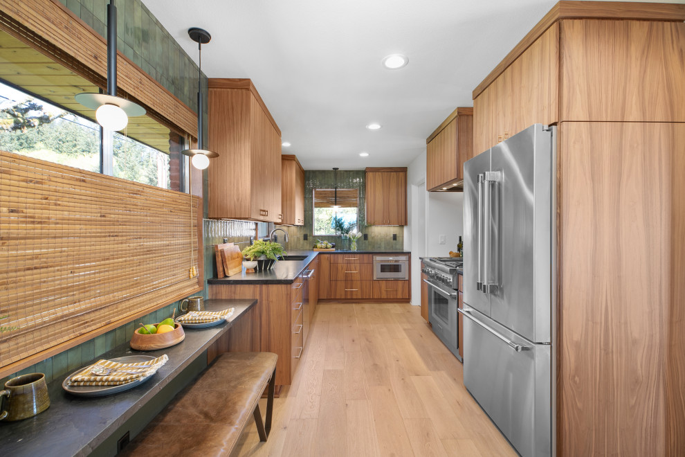 Inspiration for a mid-sized midcentury galley eat-in kitchen in Portland with a drop-in sink, flat-panel cabinets, medium wood cabinets, granite benchtops, green splashback, porcelain splashback, stainless steel appliances, light hardwood floors, no island and black benchtop.