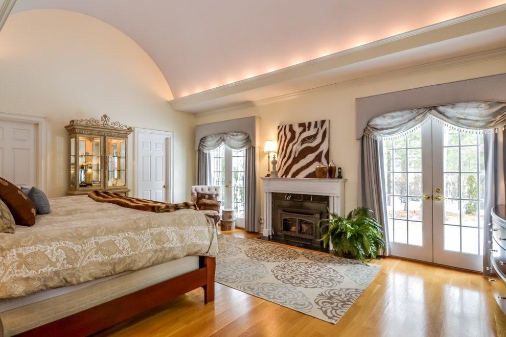 Photo of a large traditional master bedroom in New York with beige walls, medium hardwood floors, a standard fireplace, a metal fireplace surround and brown floor.