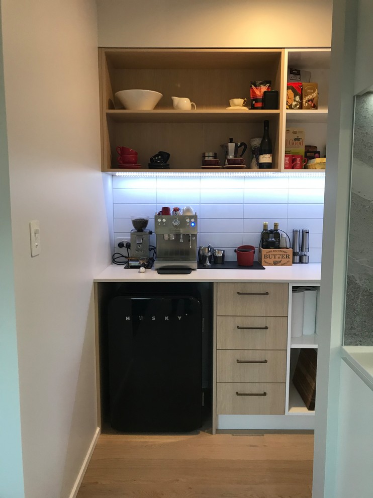 Photo of a large contemporary galley open plan kitchen in Christchurch with a single-bowl sink, flat-panel cabinets, white cabinets, quartz benchtops, grey splashback, stone slab splashback, stainless steel appliances, medium hardwood floors, with island, brown floor and white benchtop.