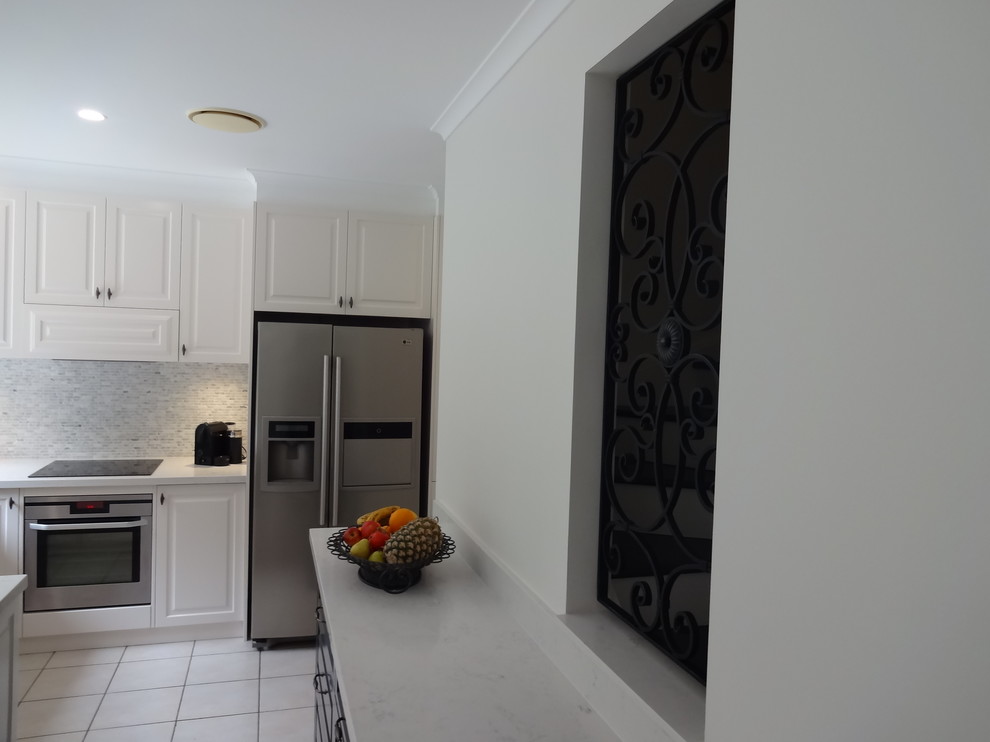 Mid-sized mediterranean eat-in kitchen in Wollongong with a drop-in sink, shaker cabinets, white cabinets, quartz benchtops, grey splashback, stone tile splashback, stainless steel appliances, ceramic floors and with island.