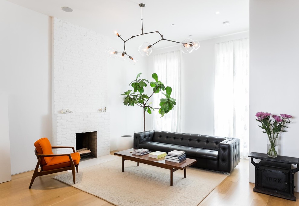 This is an example of a scandinavian open concept living room in New York with white walls, light hardwood floors, a standard fireplace, a brick fireplace surround and no tv.