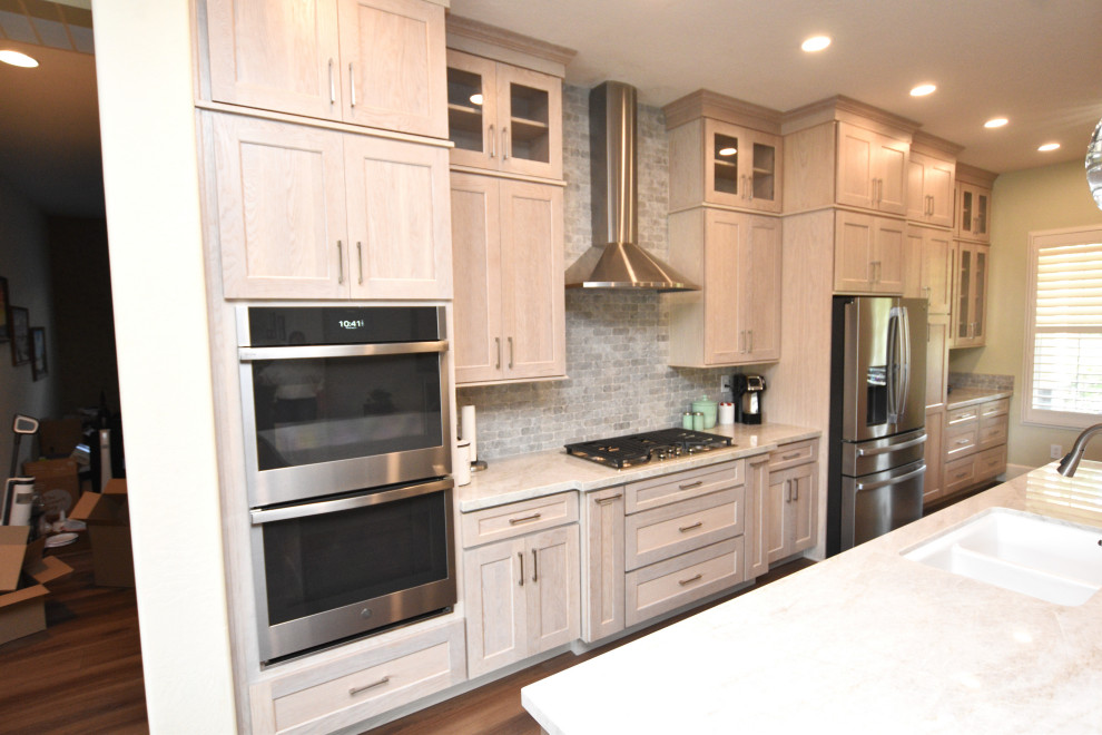 Example of a large transitional vinyl floor kitchen design with an undermount sink, shaker cabinets, light wood cabinets, quartzite countertops, multicolored backsplash, porcelain backsplash, stainless steel appliances, an island and beige countertops