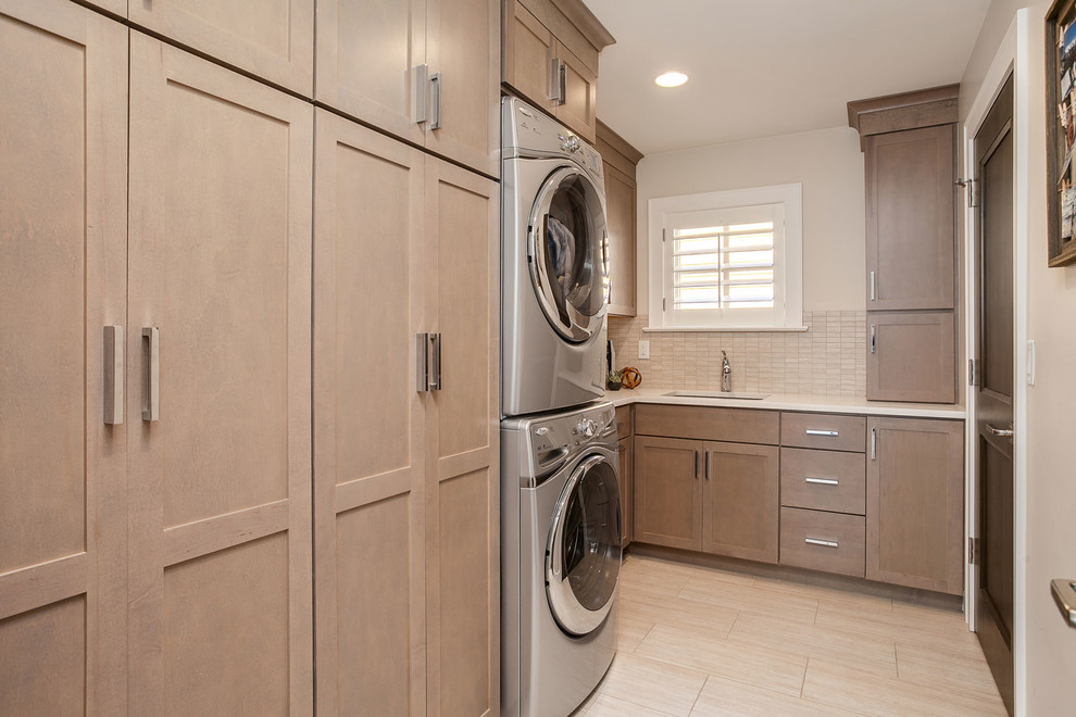 Mid-sized contemporary l-shaped dedicated laundry room in Denver with an undermount sink, shaker cabinets, medium wood cabinets, quartz benchtops, beige walls and a stacked washer and dryer.