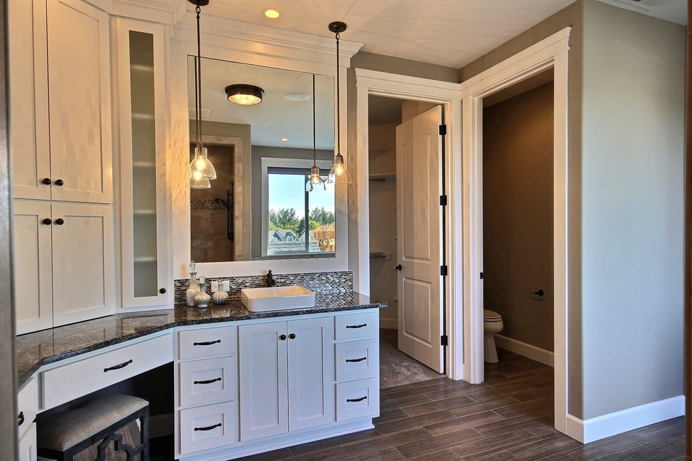 This is an example of a mid-sized transitional master bathroom in Portland with recessed-panel cabinets, dark wood cabinets, a two-piece toilet, brown tile, porcelain tile, beige walls, porcelain floors, granite benchtops, a drop-in tub, an alcove shower and a vessel sink.
