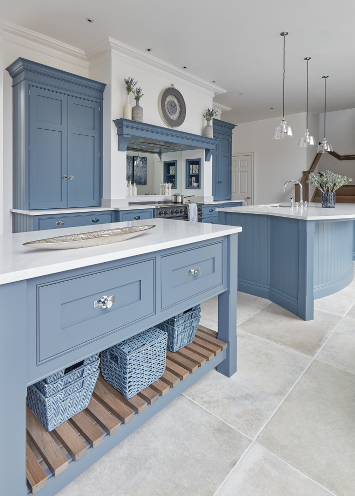 This is an example of a large traditional l-shaped eat-in kitchen in Gloucestershire with an undermount sink, shaker cabinets, blue cabinets, quartz benchtops, white splashback, mirror splashback, stainless steel appliances, limestone floors, multiple islands, beige floor and white benchtop.