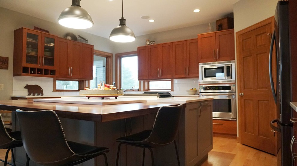 Large transitional l-shaped medium tone wood floor open concept kitchen photo with an undermount sink, recessed-panel cabinets, brown cabinets, white backsplash, subway tile backsplash, stainless steel appliances, an island and white countertops