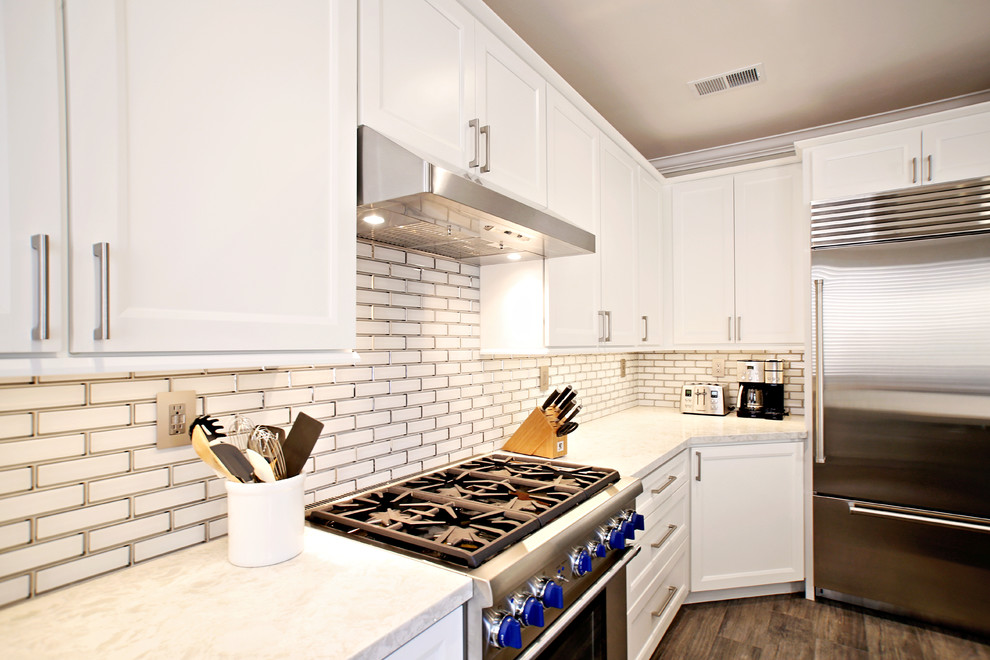 Photo of a mid-sized transitional u-shaped eat-in kitchen in San Diego with a farmhouse sink, shaker cabinets, grey cabinets, quartz benchtops, white splashback, subway tile splashback, stainless steel appliances, light hardwood floors, with island, brown floor and white benchtop.