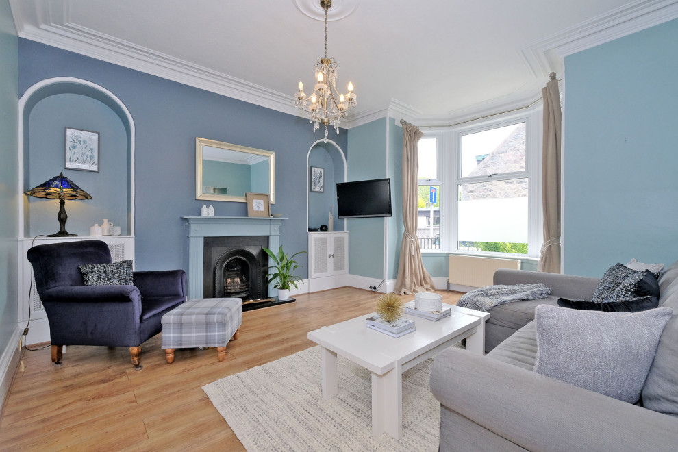 Mittelgroßes Klassisches Wohnzimmer mit blauer Wandfarbe, Laminat, Kamin, Kaminumrandung aus Holz, TV-Wand und braunem Boden in Sonstige