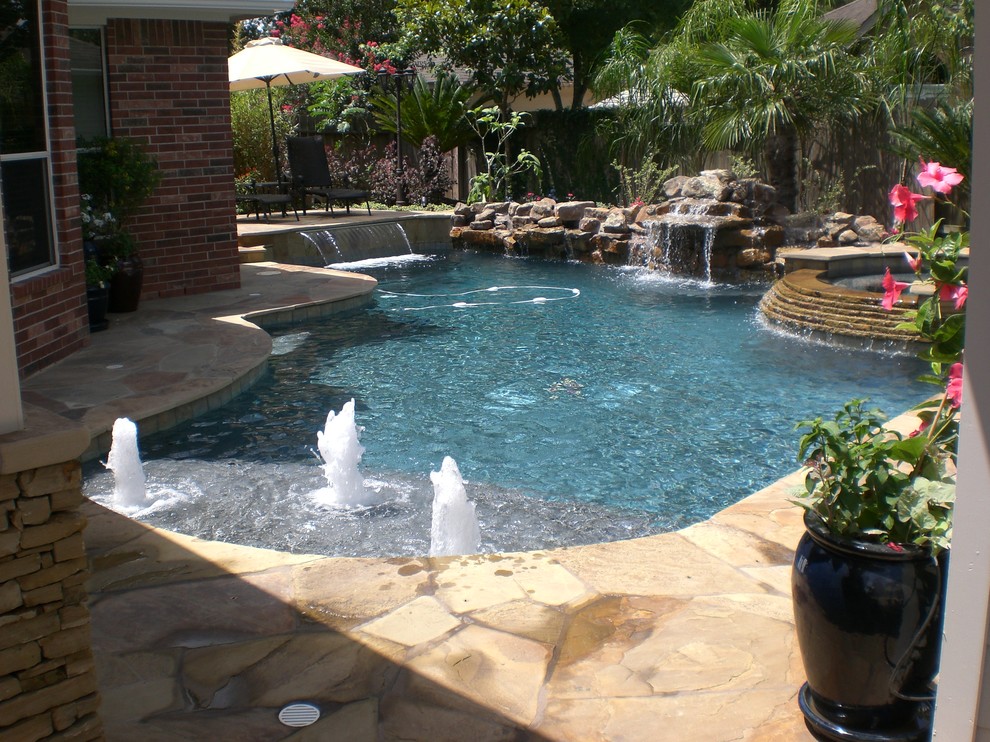 This is an example of a mid-sized traditional backyard custom-shaped pool in Houston with natural stone pavers and a hot tub.