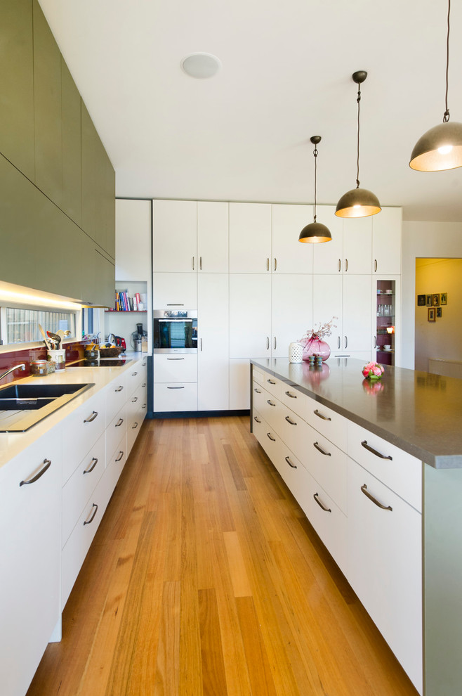Photo of a large transitional l-shaped open plan kitchen in Melbourne with a double-bowl sink, flat-panel cabinets, white cabinets, red splashback, light hardwood floors, with island, quartz benchtops, glass sheet splashback, stainless steel appliances, brown floor and brown benchtop.