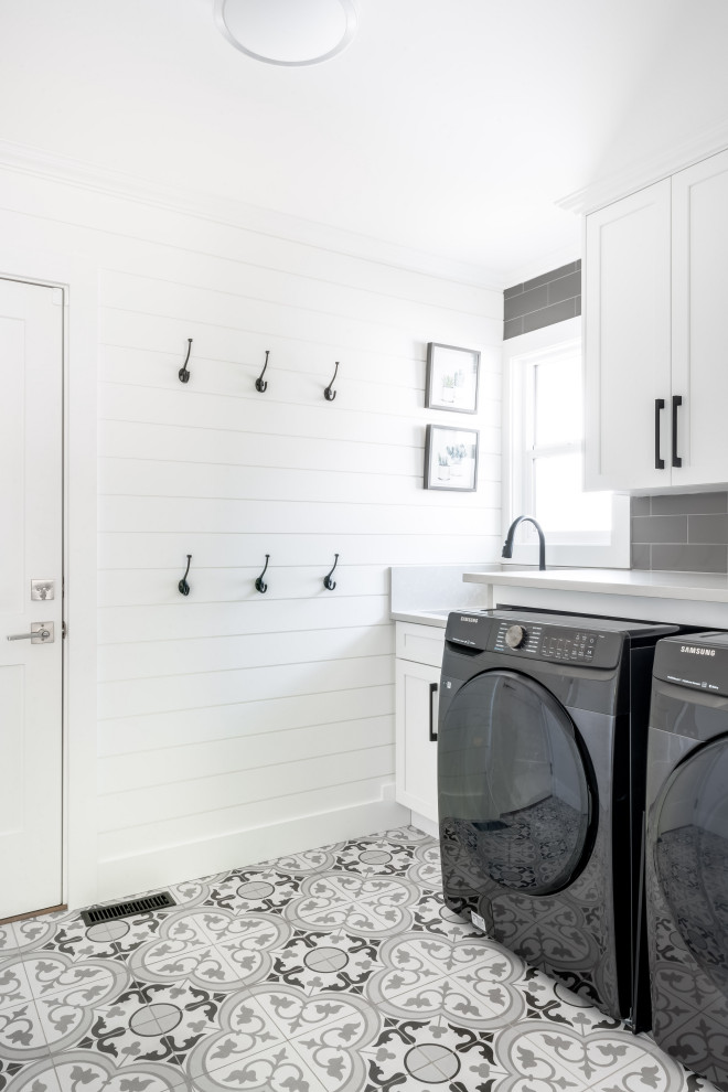 Foto på en mellanstor lantlig grå linjär tvättstuga enbart för tvätt, med en nedsänkt diskho, skåp i shakerstil, vita skåp, bänkskiva i kvarts, grått stänkskydd, stänkskydd i keramik, vita väggar, klinkergolv i keramik, en tvättmaskin och torktumlare bredvid varandra och vitt golv