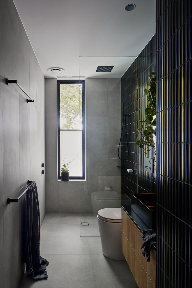 Inspiration for a mid-sized industrial 3/4 bathroom in Melbourne with flat-panel cabinets, medium wood cabinets, black tile, a vessel sink, grey floor, black benchtops, a single vanity and a floating vanity.
