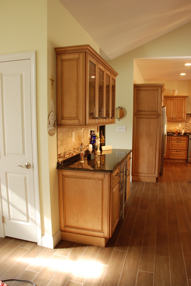 Mid-sized transitional l-shaped ceramic tile eat-in kitchen photo with a farmhouse sink, raised-panel cabinets, medium tone wood cabinets, granite countertops, beige backsplash, ceramic backsplash, stainless steel appliances and an island